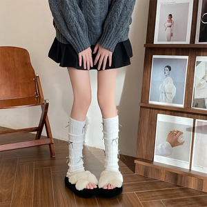 Close-up of white knitted leg warmers featuring grey ribbon bows in a cozy home setting