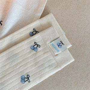 Dettaglio calzini in cotone beige a coste con ricamo ciliegia blu ed etichetta brand