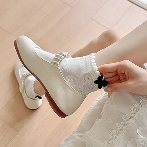 Close-up of beige Mary Jane flats with ruffled straps and lace bow socks on wood floor