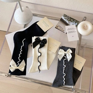 Dettaglio di calzini con fiocco in nero bianco e grigio con trame a maglia a coste