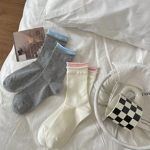 Detail of ribbed mid-tube socks in gray and beige with contrast rolled edges on bed