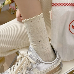 Close-up of beige frilly socks with colorful speckled knit texture and wavy cuffs