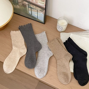 Detail of five pairs of frilled cotton blend socks in neutral tones on a wooden surface