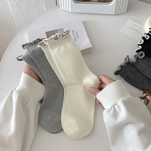 Detail of ruffled edges on rib-knit cotton socks in cream and light grey colors