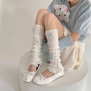 Detail of cream knit leg warmers with heart cut-outs and blue ribbon bow accents