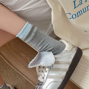 Detail of grey knitted mid-tube socks with sky blue cuffs and silver metallic sneakers