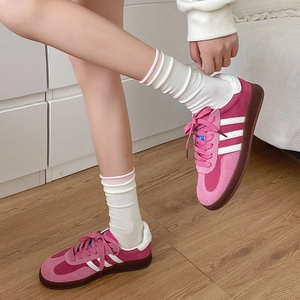 Close-up of pink suede sneakers with white stripes on a wooden floor, ballet aesthetic style