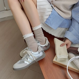 Detail of beige ribbed crew socks featuring delicate white lace trim and wood floor background