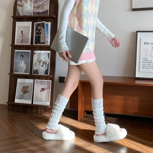 Close-up of white knitted leg warmers with pink ribbons and plush slippers