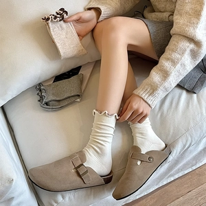 Close-up of white ruffled crew socks paired with beige suede clogs for a cozy aesthetic
