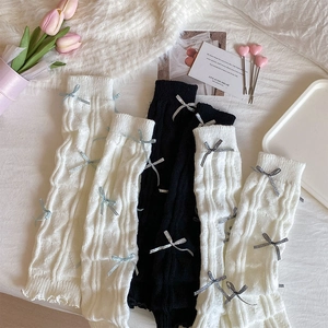 Close-up of knit leg warmers featuring ribbon bows and ruffled edges in soft lighting
