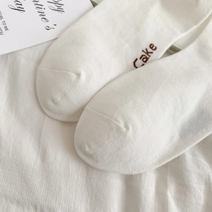 Close-up of white knitted cotton socks with brown Cake letter embroidery detail