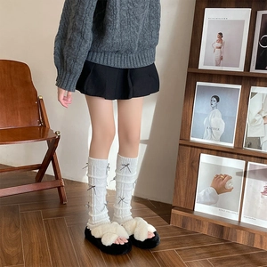 Close-up of cable knit leg warmers with grey bows and plush platform slippers on wooden floor
