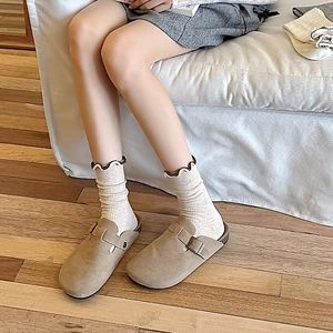 Detail of light brown suede clogs with adjustable metal buckle and ruffle edge socks