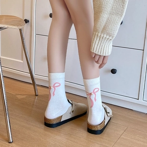 Détail de chaussettes blanches avec nœud rose et perle portées par un mannequin