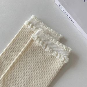 Detail of off-white knit socks featuring vertical stripes and ruffled lettuce edge cuffs