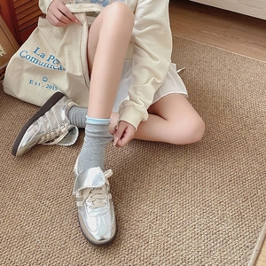 Top view of silver metallic sneakers with white laces on a brown woven carpet texture
