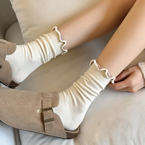 Close-up of white ribbed crew socks with scalloped edges and brown trim details