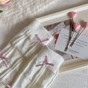 Close-up of white cable knit leg warmers with delicate lavender ribbon bows