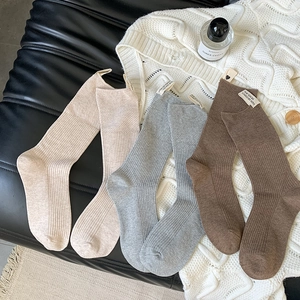 Dettaglio di tre paia di calze in maglia a coste beige, grigie e marroni con etichetta in tessuto