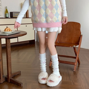 Close-up of white knit leg warmers featuring pink silk bows and delicate hollow-out texture