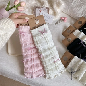 Detailed knit texture of pink leg warmers featuring delicate ribbon bows and brand tags