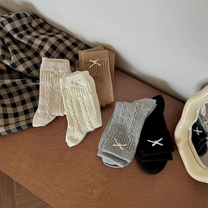 Close-up of cable knit crew socks with delicate bow accents in neutral colors