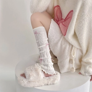 Close-up of white balletcore leg warmers with pink bows and knitted heart patterns