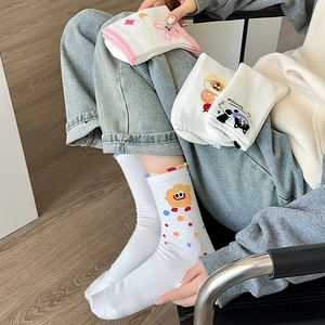 Close-up of white crew socks featuring cartoon bear embroidery and colorful frill cuffs