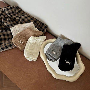 Detail showing five pairs of cable knit socks with bow and pearl accents on a wooden desk