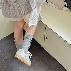 Dettaglio calzini grigi a costine con etichetta in tessuto e scarpe da ginnastica bianche