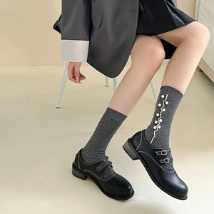 Close-up of grey knit socks with white wavy trim and pearls worn with black Mary Jane shoes