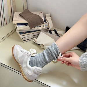 Dettaglio calzini grigi a coste con etichetta bianca e sneakers bianche retrò