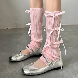 Detail of pink knitted leg warmers with satin bows and silver Mary Jane shoes