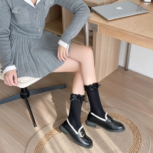 Dettaglio di calze Lolita nere con bordo in pizzo e fiocchi abbinate a mocassini