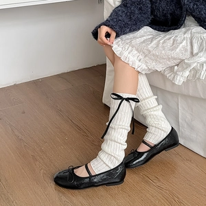 Détail de jambières en tricot crème avec des nœuds en satin noir de style balletcore