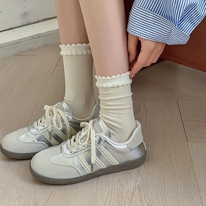 Close-up of white ruffled crew socks with ribbed texture paired with silver fashion sneakers