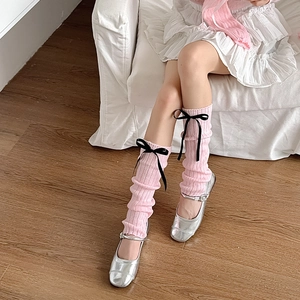 Détail de jambières en tricot rose avec nœuds en ruban noir et maille côtelée