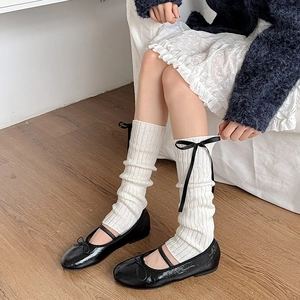 Gros plan de jambières en tricot blanc avec nœuds noirs et chaussures Mary Jane