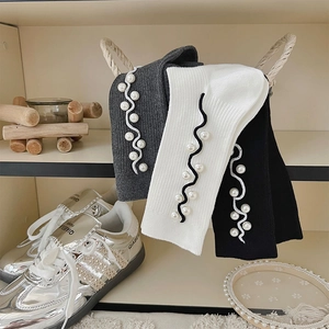 Close-up of knit socks with wavy white embroidery and elegant pearl accents in three colors