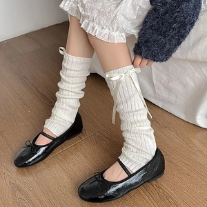 Détail de jambières en tricot blanc avec nœuds et chaussures Mary Jane noires