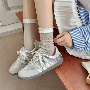 Close-up of white lace ruffle socks paired with silver metallic sneakers and pleated skirt