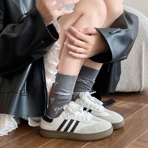 Detail von Ballet-Schleifensocken mit cremefarbenen Retro-Sneakern auf Holzboden