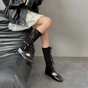 Detail of black knit leg warmers with ribbon lacing and matching ballet flat shoes