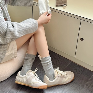 Dettaglio di calze grigie a coste con etichetta in tessuto e sneakers bianche