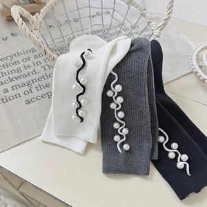 Close-up of ribbed knit socks with wavy ribbon trim and faux pearl beads in soft lighting