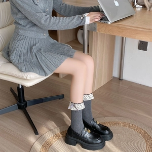 Detail of grey ribbed mid-calf socks with lace trim and bow paired with black loafers