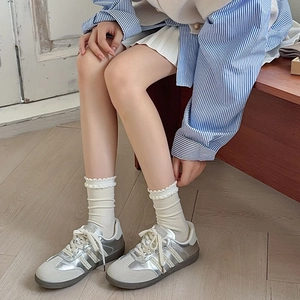 Detail of white lace ruffle socks paired with retro silver sneakers on wooden floor