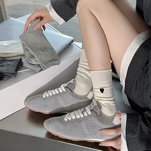 Detailed view of beige vertical ribbed socks with black heart embroidery and sneakers