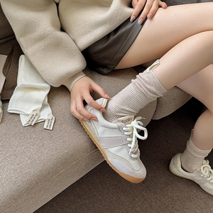 Dettaglio di calze a costine con sneakers GAT beige su un divano grigio scuro